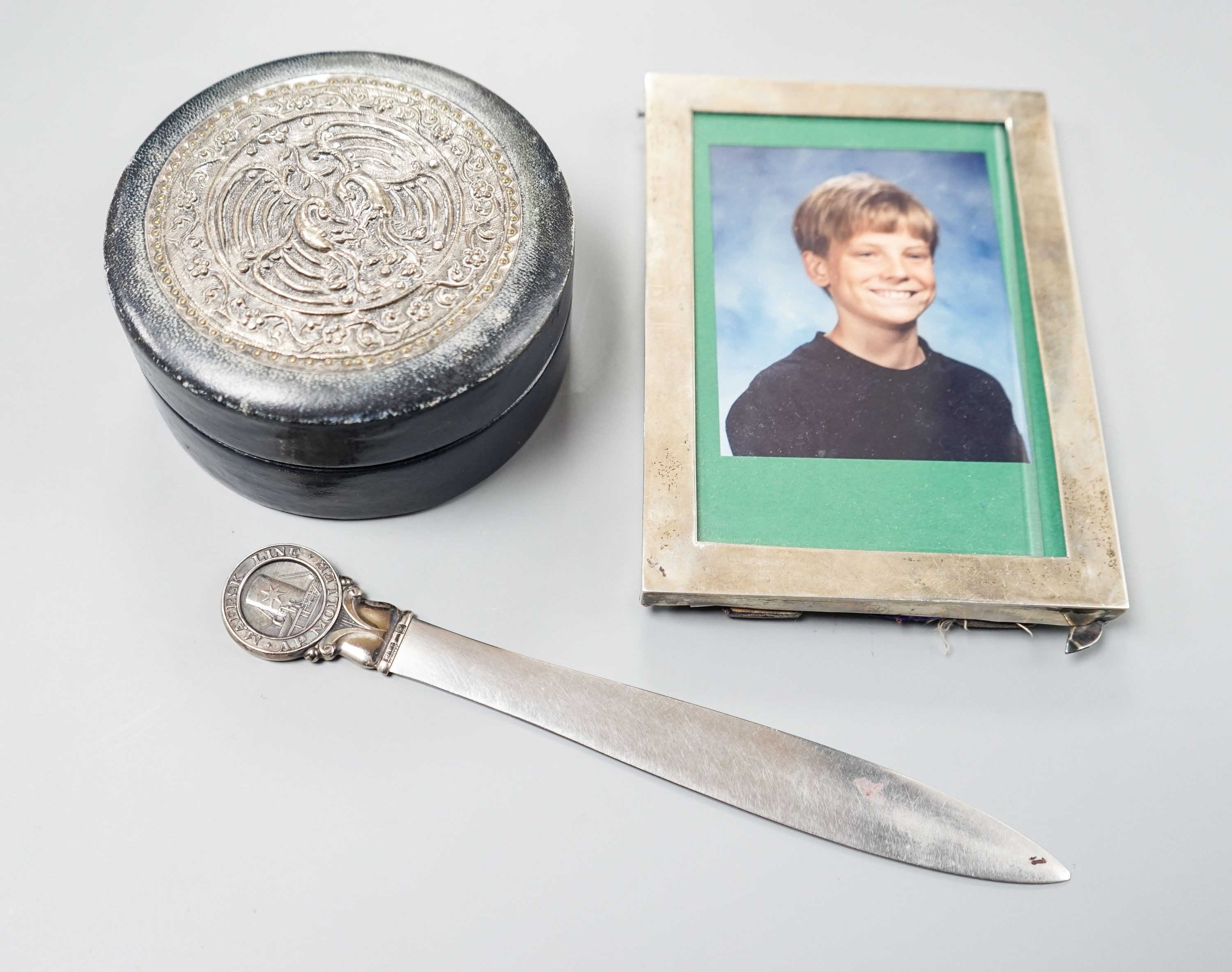 An Edwardian silver mounted photograph frame, 15.5cm, a letter opener with white metal finial and blue leather stud box with Far Eastern embossed white metal panel to lid.